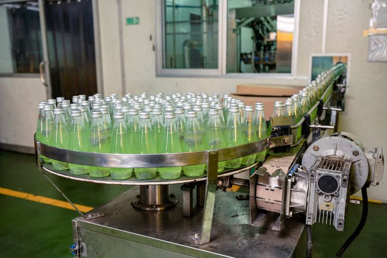 Línea de producción de bebidas con botellas en transportador industrial en planta de manufactura