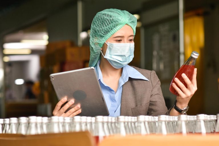 Inspector de calidad en planta de bebidas revisando botella con tableta digital para control de proceso