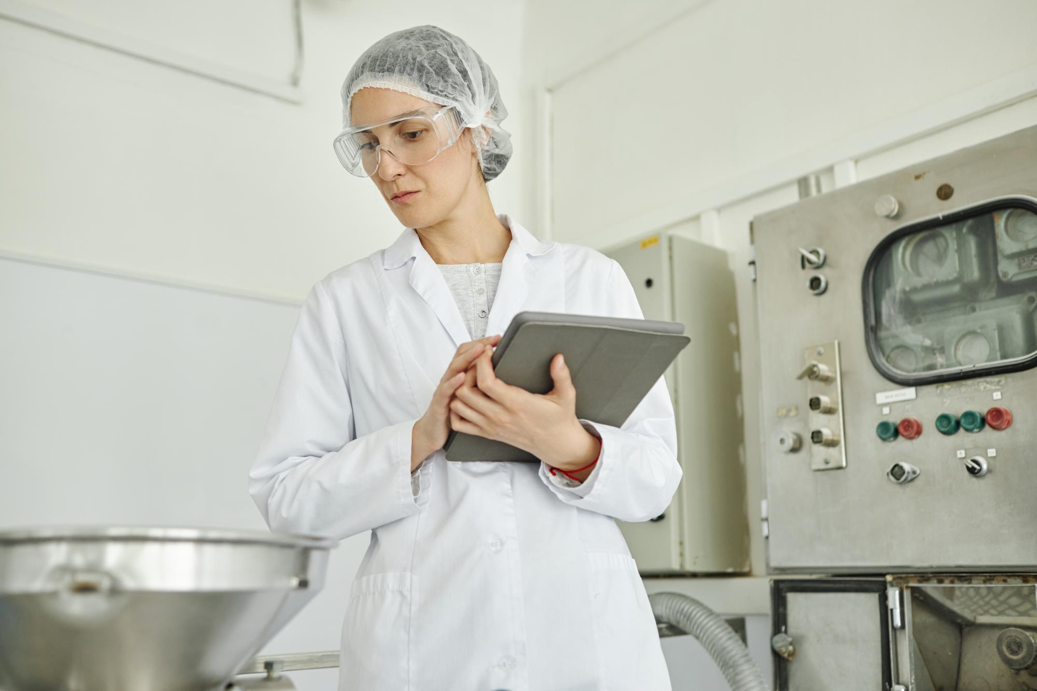 Operador de planta industrial consultando métricas de producción en tableta frente a panel de control